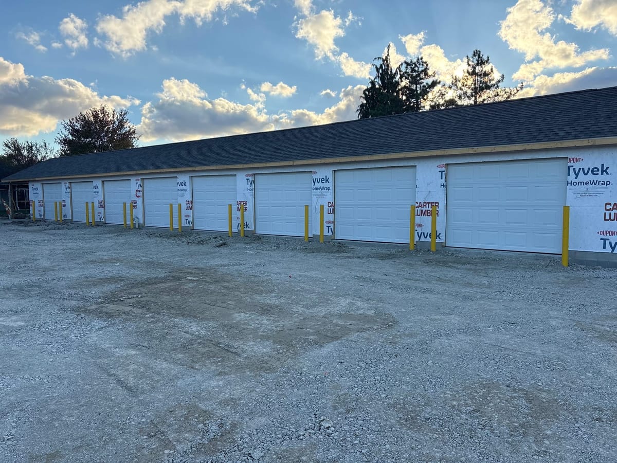 Row of new white sectional garage doors installed across a commercial storage building under construction