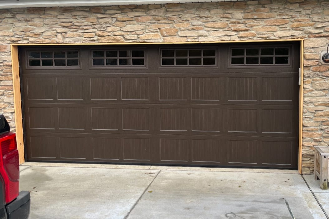 New brown carriage-style double garage door with a row of windows on a stone-front home