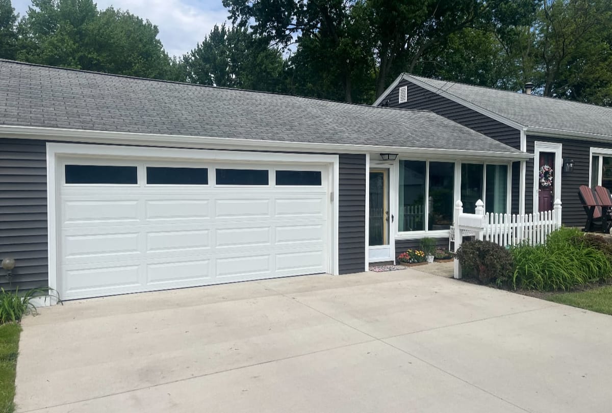 New white double garage door with a window row on a gray ranch-style home