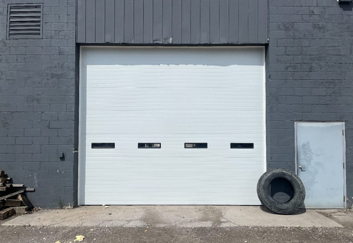 White commercial sectional door with window panels installed on a gray block shop building